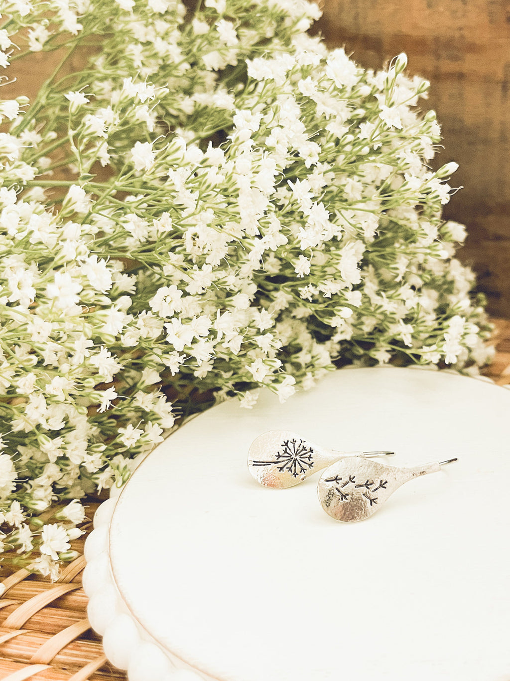 White flowers with a decorative plate and earrings on a woven surface