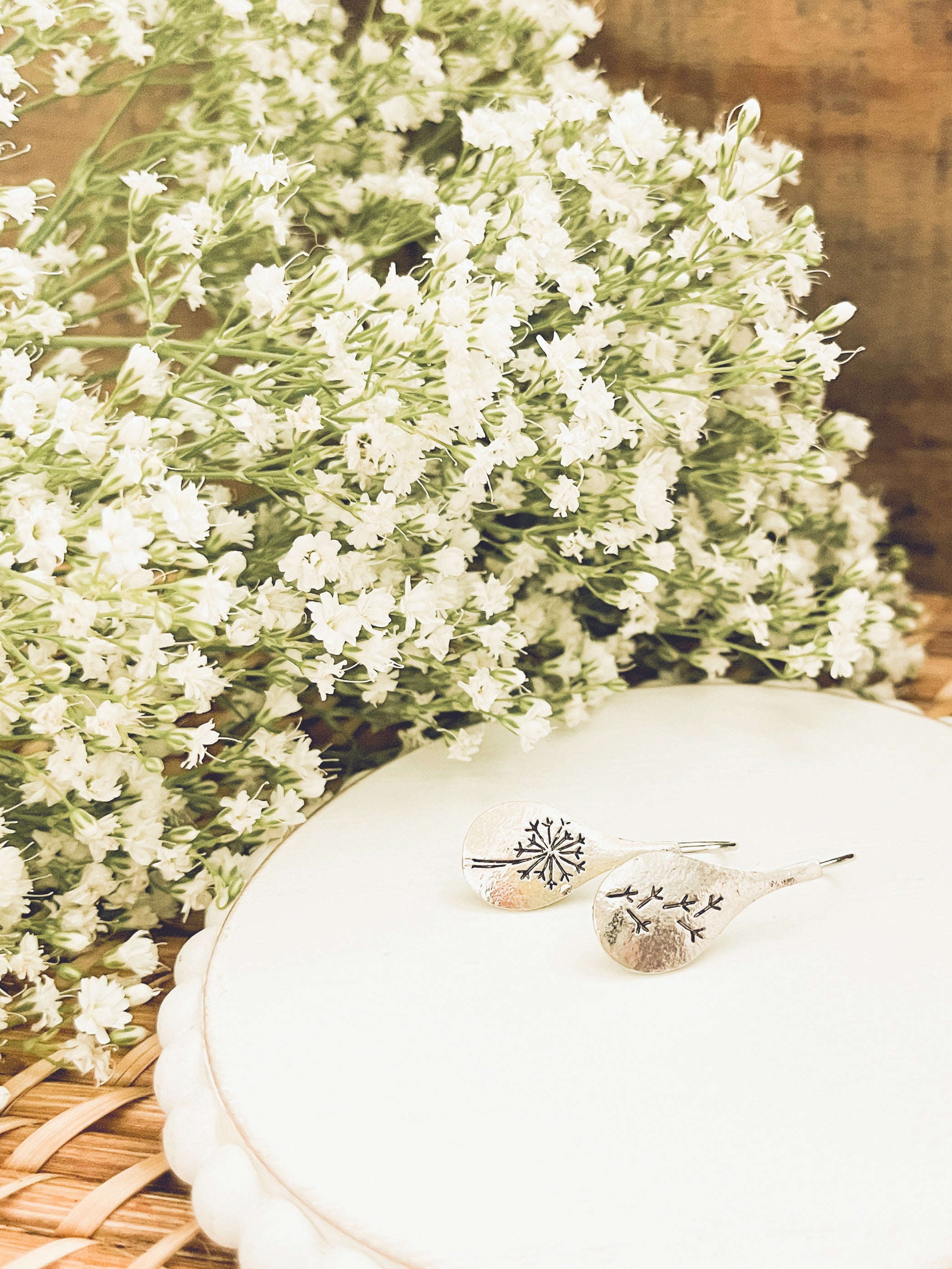 White flowers with a decorative plate and earrings on a woven surface