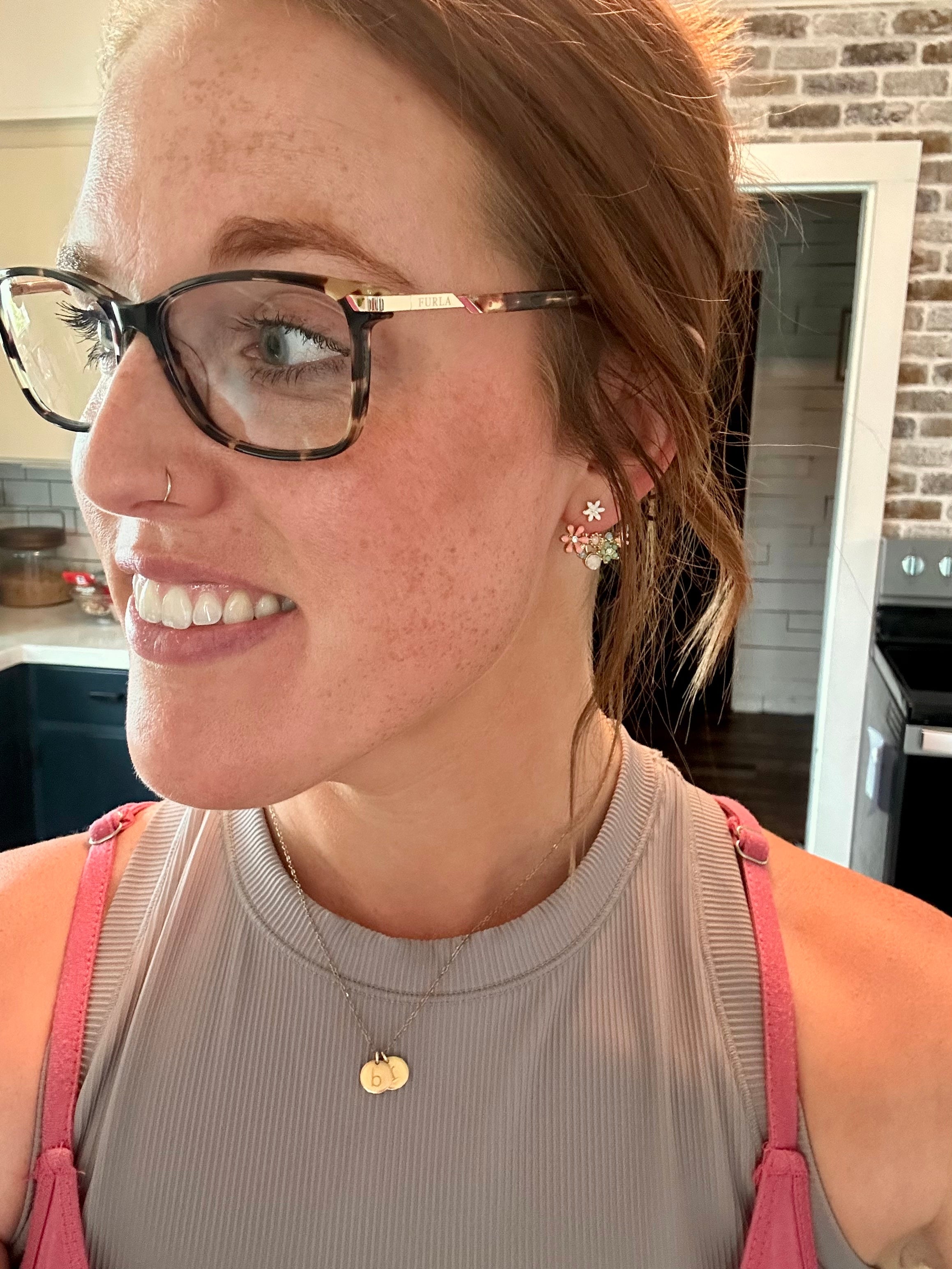 Woman wearing glasses and a gray tank top with pink straps in a kitchen.