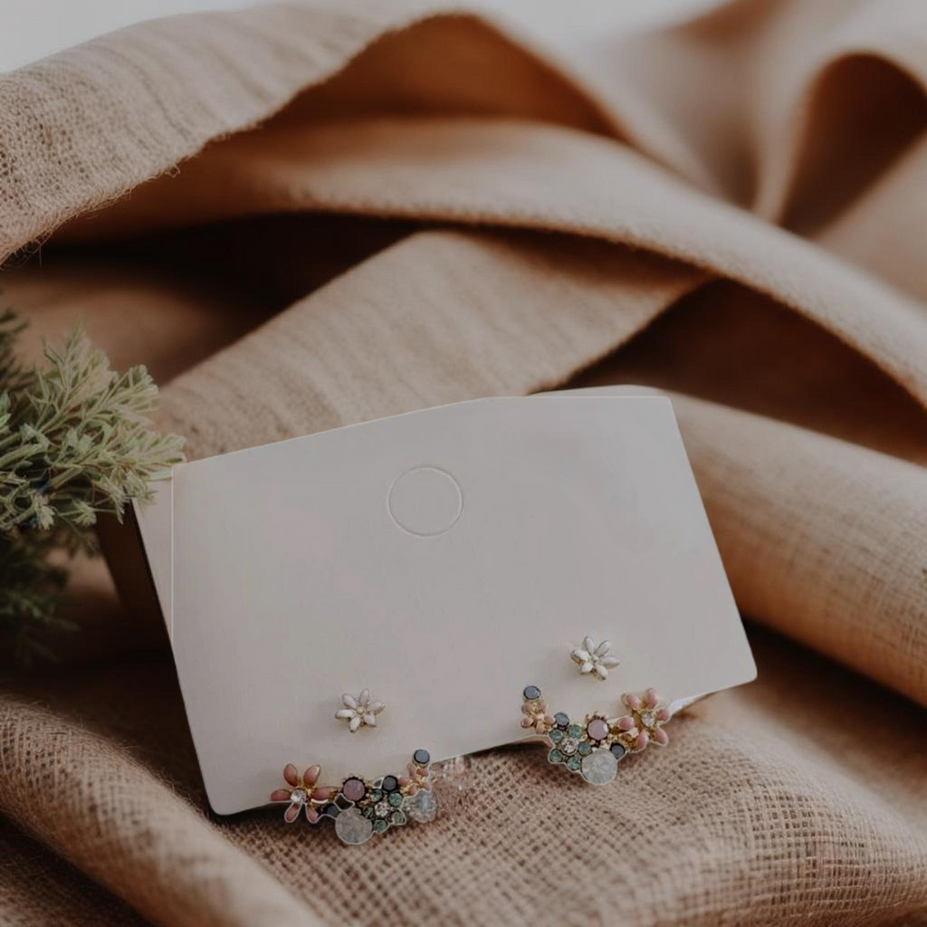 Pair of floral earrings on a white card with a beige fabric background