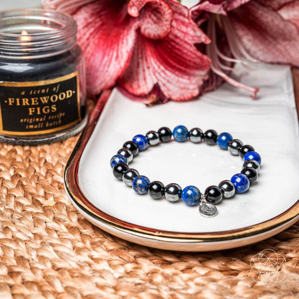 Bracelet with blue and black beads on a white dish next to a candle labeled 'Firewood Figs'.