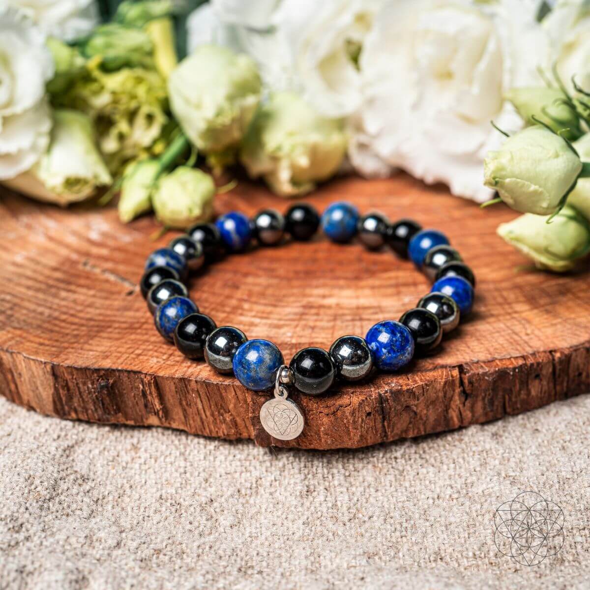 Beaded bracelet with blue and black stones on a wooden surface with flowers in the background